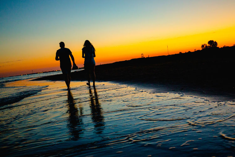 Silhouette couple on beach against sky during sunset