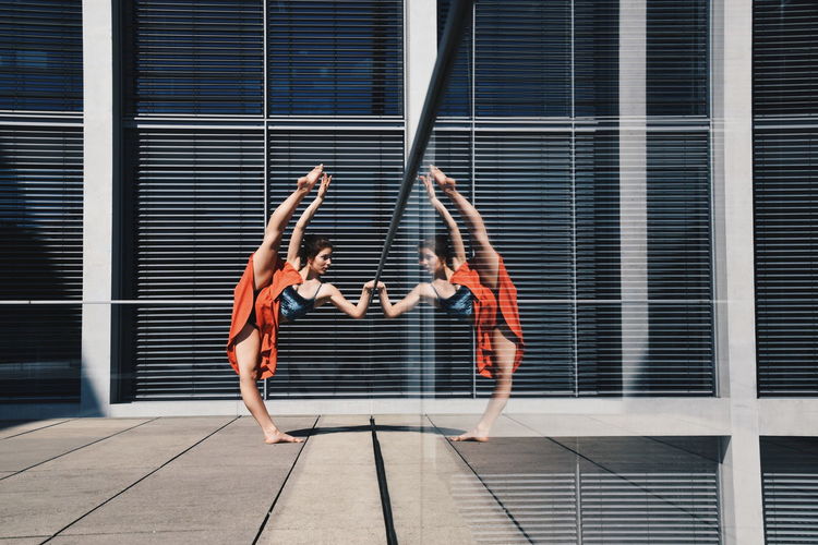 Full length of woman doing gymnastics on floor with reflection in glass window of building