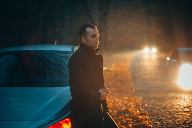 Man looking away while standing in car at night