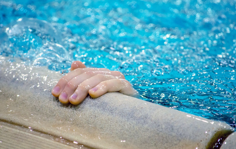 A small hand reaches out of a swimming pool to grasp the edge perhaps to keep from drowning