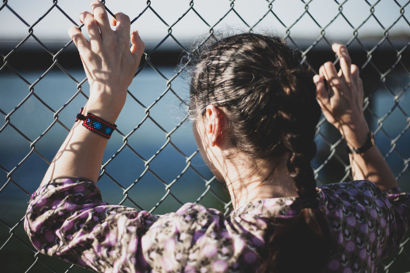 Rear view of woman looking through woman chainlink fence