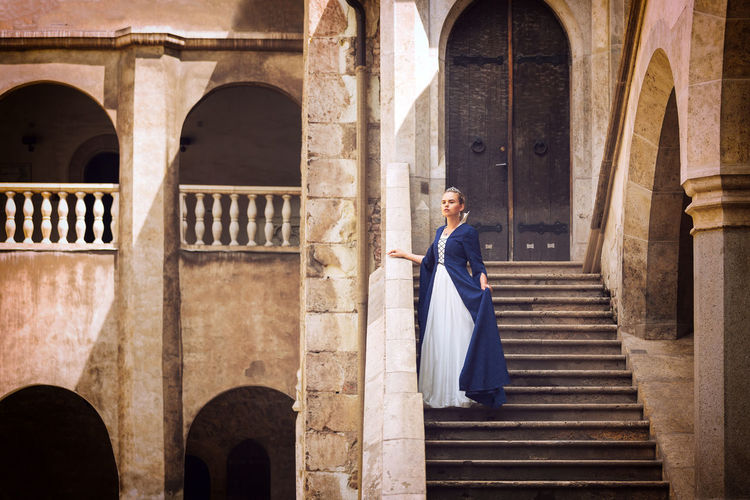 Young beautiful princess or queen standing on steps of medieval castle