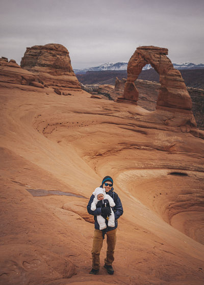 A man with a child is standing near delicate arch at arches np