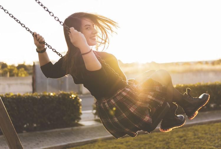 Young woman sitting on swing against sky during sunset