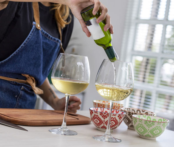 Midsection of woman pouring wine in glass on table