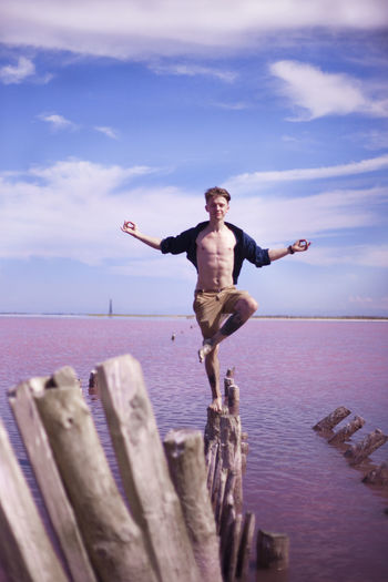 Full length of man standing on wooden log against sea and sky