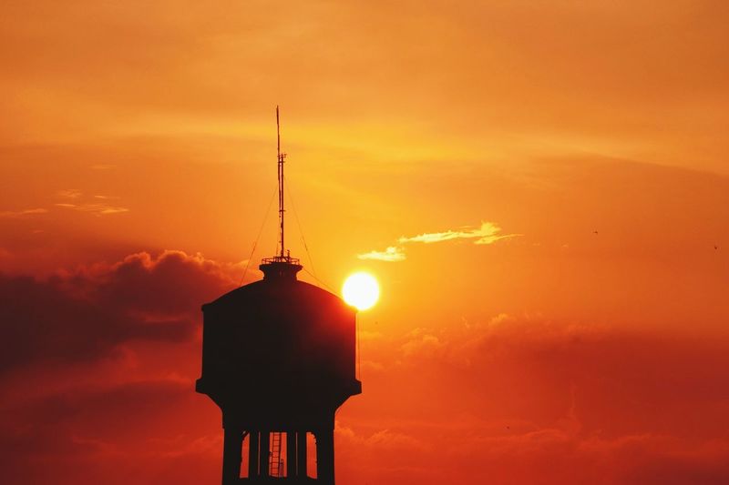 Low angle view of water tower against orange sky