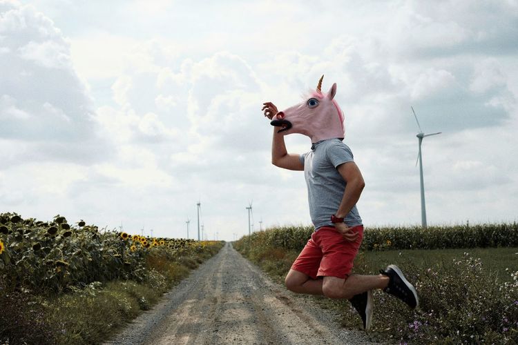 Man wearing horse mask while jumping over road against sky