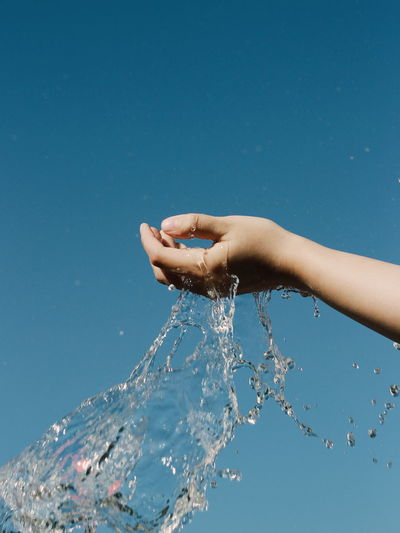 Close-up of hand splashing water against clear blue sky