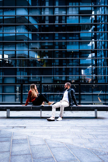 Man and woman sitting on seat against building in city