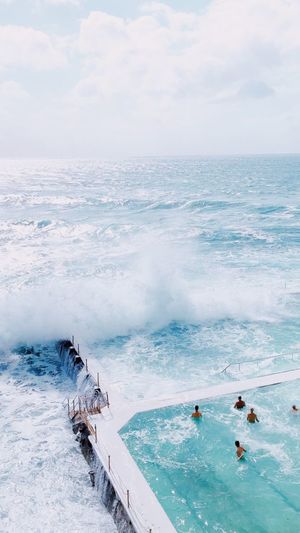 Aerial view of people enjoying in swimming pool by sea