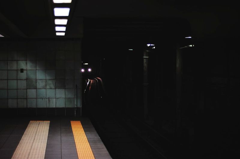 Rear view of man standing at illuminated subway station