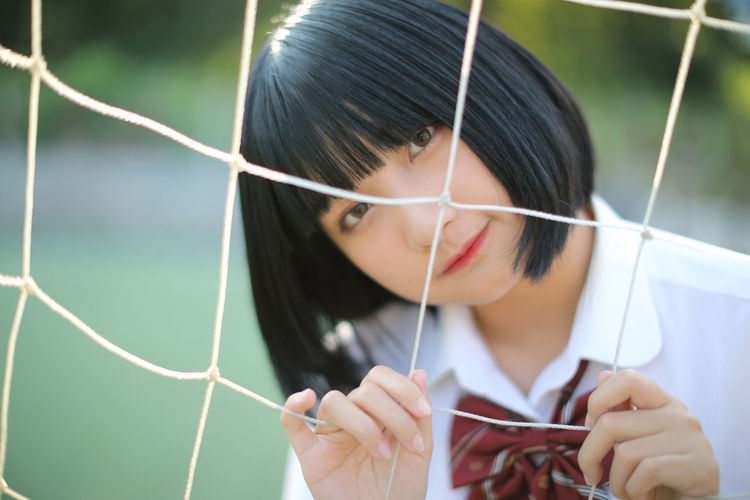 Portrait of young woman standing by sports net