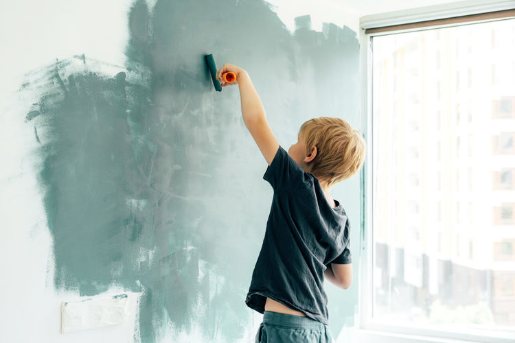 Rear view of boy painting on wall at home