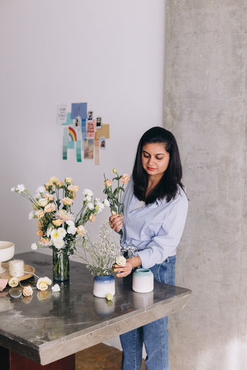 Florist standing in front of a marble table making a flower arrangement 