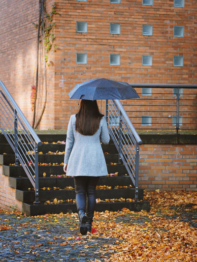 Rear view of woman walking on wet umbrella during autumn