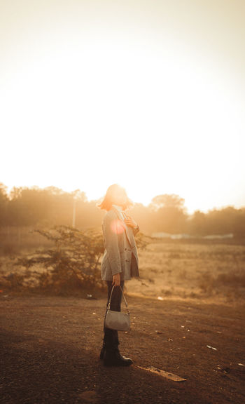 Rear view of woman walking on field against sky during sunset