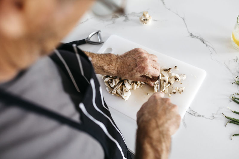Man cutting mushrooms on cutting board at kitchen counter