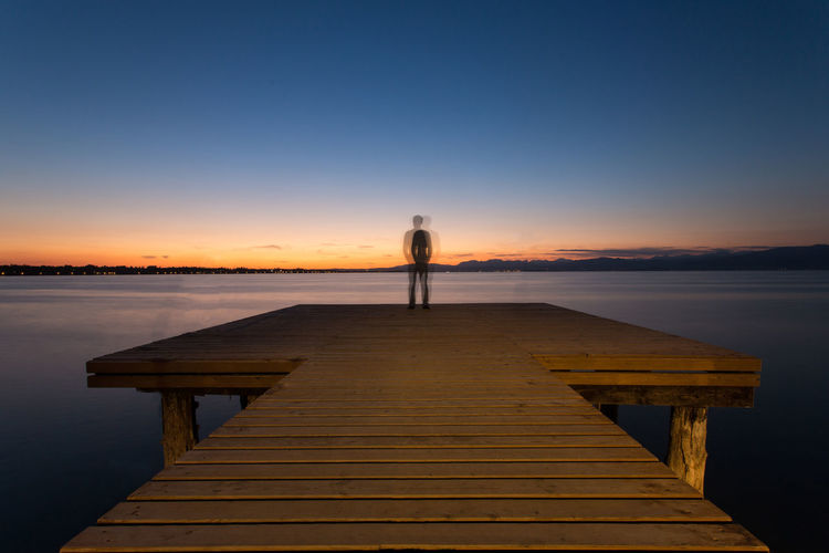 Man on pier against romantic sky at sunset