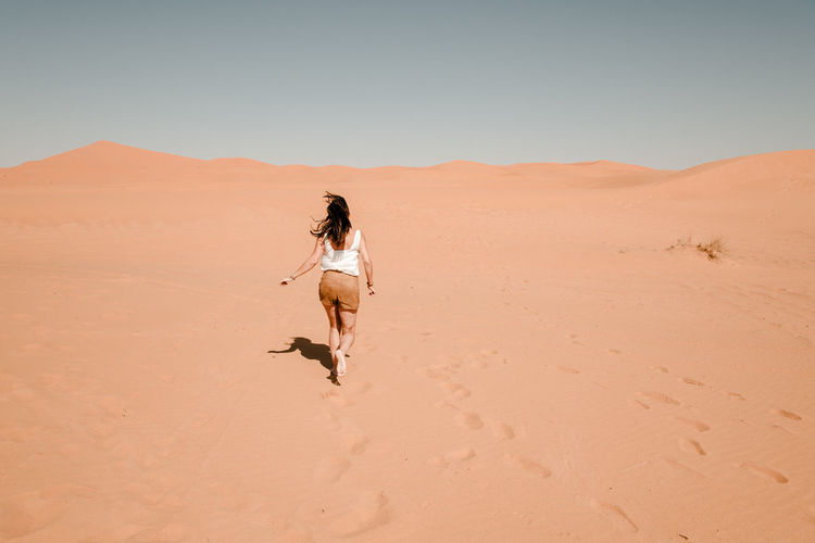 Full length of man on sand dune in desert against clear sky