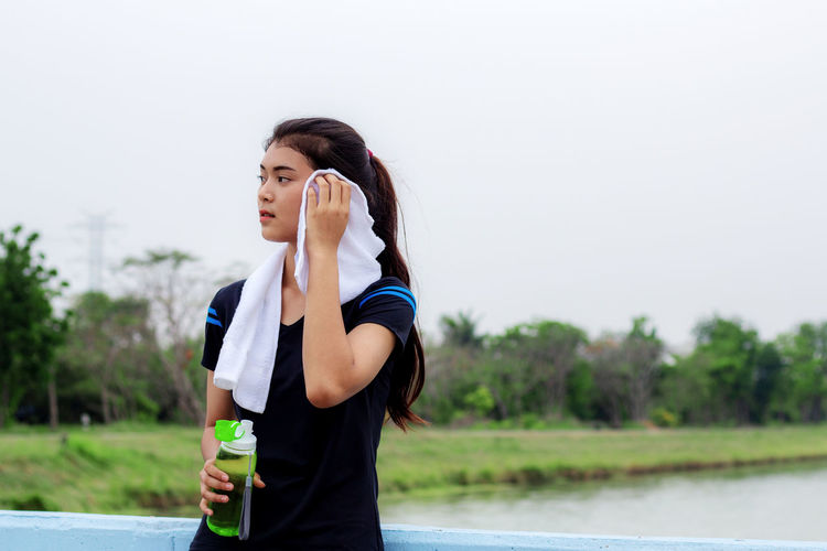 Side view of young woman drinking water against clear sky
