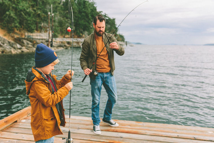 Father and son holding fishing rods while standing by sea