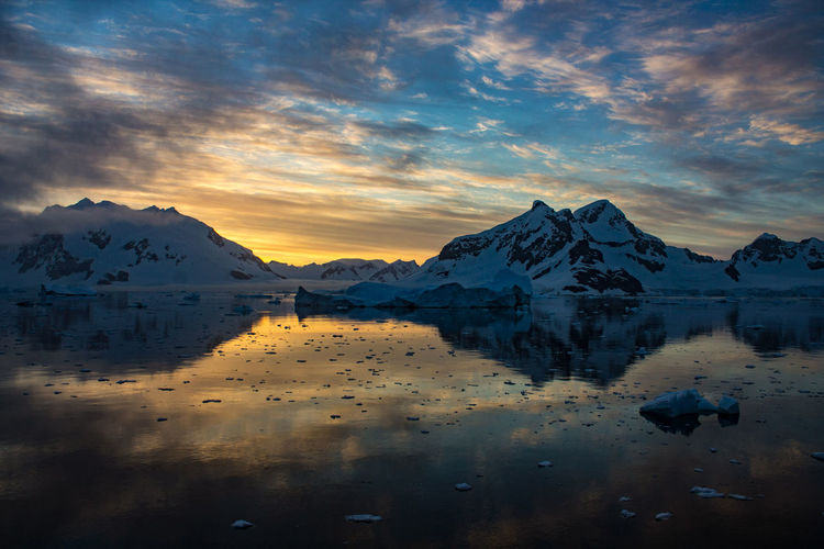 Colorful summer sunset in antarctica over snowy mountains and sea with icebergs.