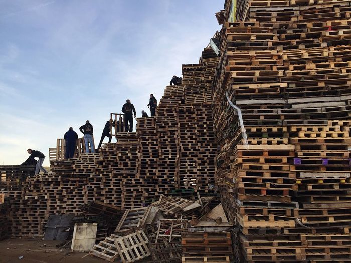 Workers arranging wooden palettes against sky