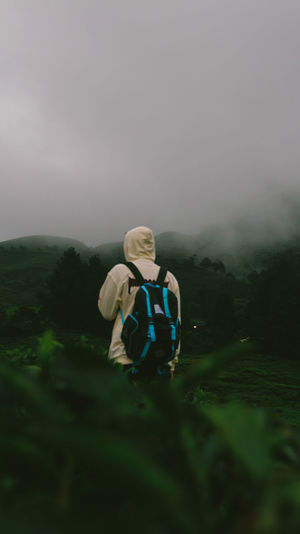Rear view of backpack man standing on field against dramatic sky