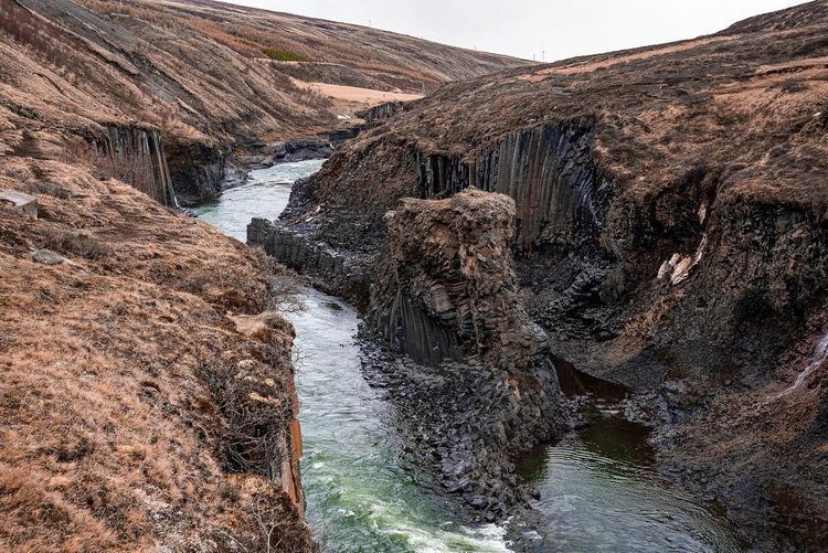 Stream flowing amidst basalt columns rock formation at eastfjords against sky