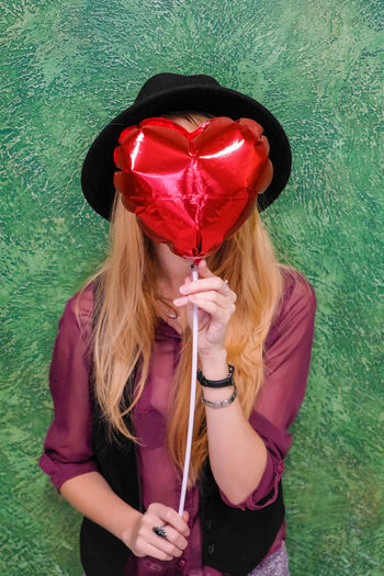 Midsection of woman holding red heart shape against wall