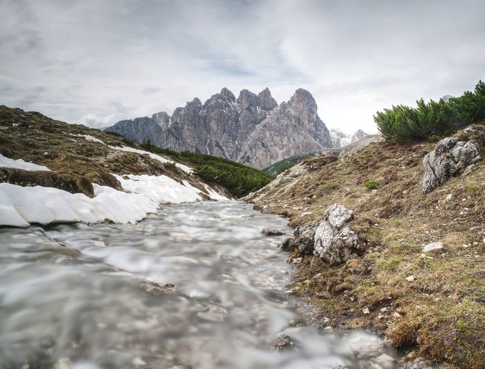 The mountain river against the sharp mountains in dolomites. water come from thawing snow or glacier