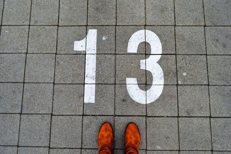 Low section of person wearing shoes by number 13 on footpath