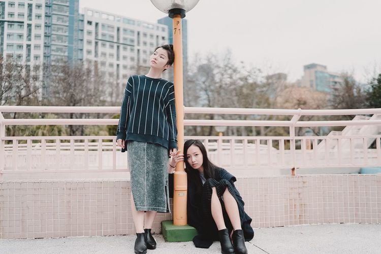 Sad friends on footbridge against sky in city