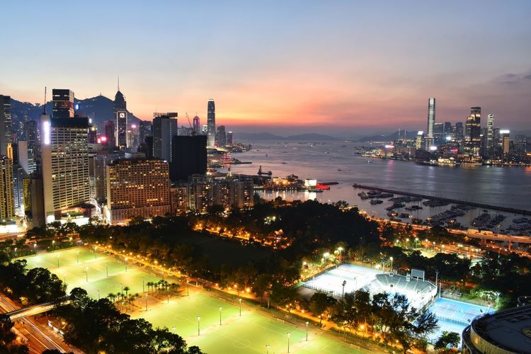 Illuminated city by sea against sky during sunset
