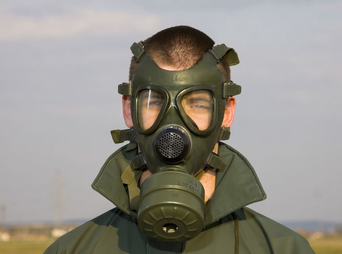 Portrait of man wearing gas mask standing against sky