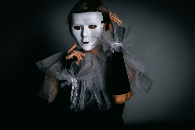 Woman in white theater mask and harlequin collar on black background. fancy dress, masquerade 