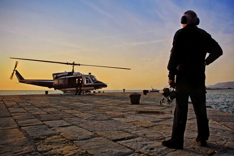 Full length rear view of military worker standing by helicopter at port during sunset