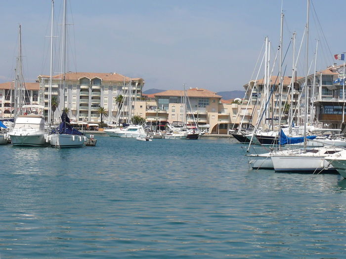 Boats moored at harbor by houses against sky