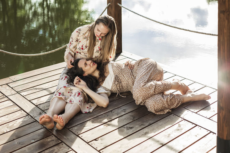 Woman talking with friend lying on lap at pier