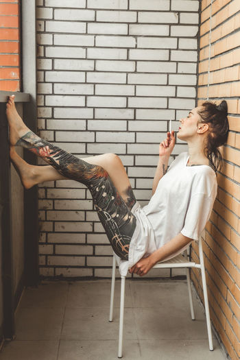 Woman sitting on chair against wall