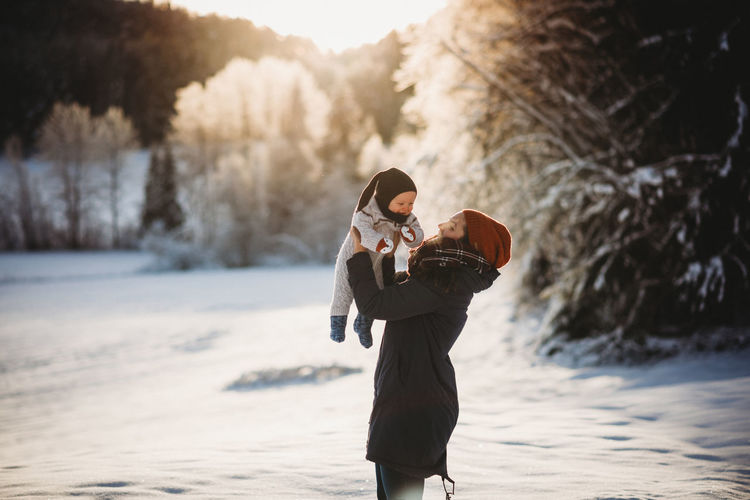 Mom holding baby up in snowy woods during sunset in norway in winter