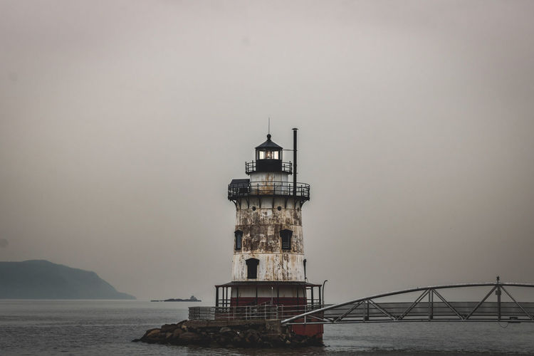 Lighthouse by the foggy sea against sky.