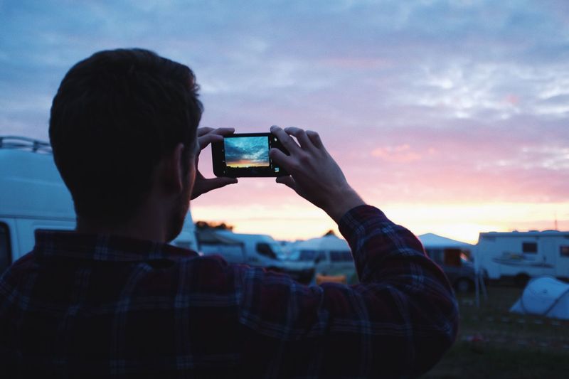 Rear view of man photographing through smart phone against sky