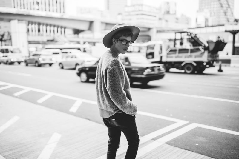Side view of young man wearing hat while standing on city street