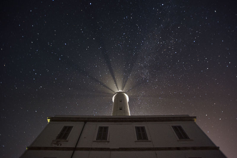 Low angle view of illuminated lighthouse against sky at night