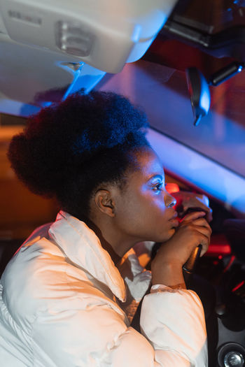 Sad depressed african woman behind steering wheel in car at night, sits at driver seat feels unhappy