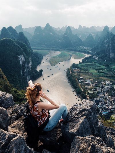 Woman sitting on rock by mountains against sky