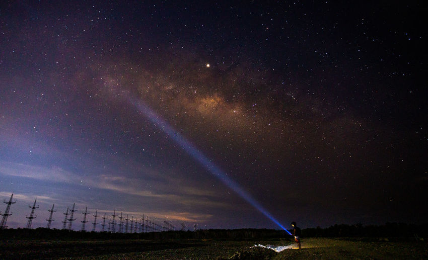 Man holding illuminated flashlight while standing on land against sky at night