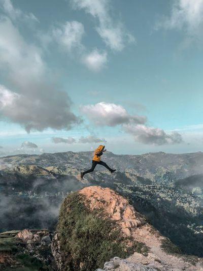 Man on rock by mountain against sky